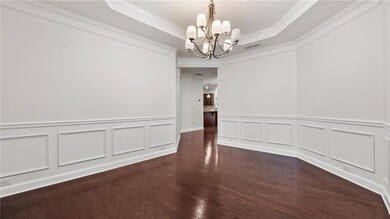 Unfurnished dining area featuring a chandelier, wainscoting, wood finished floors, crown molding, and a decorative wall