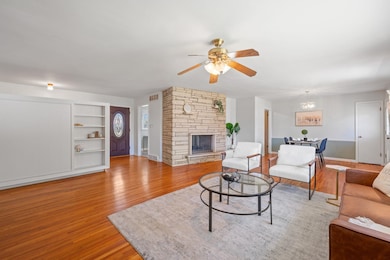 Living area with light wood-type flooring, a ceiling fan, a fireplace, and a chandelier