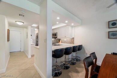 Kitchen with decorative backsplash, light tile patterned floors, a kitchen breakfast bar, white cabinets, and stacked washer and clothes dryer