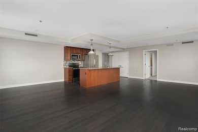 Kitchen with brown cabinets, hanging light fixtures, open floor plan, tasteful backsplash, and stainless steel appliances