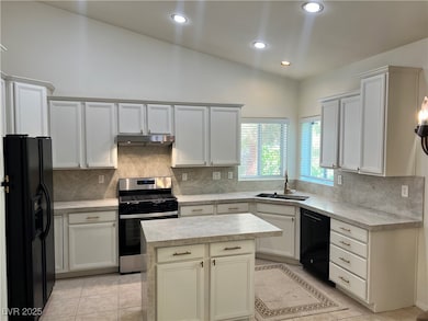 Kitchen with black appliances, decorative backsplash, lofted ceiling, recessed lighting, and white cabinets