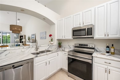 Kitchen featuring appliances with stainless steel finishes, white cabinets, light stone countertops, light tile patterned floors, and vaulted ceiling