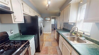 Kitchen with light tile floors, sink, rail lighting, gas range oven, and countertops dark