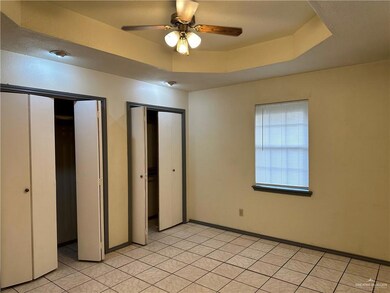 Unfurnished bedroom featuring multiple closets, a tray ceiling, light tile patterned floors, and a ceiling fan