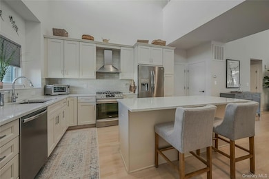 Kitchen with appliances with stainless steel finishes, backsplash, light wood-type flooring, a center island, and wall chimney range hood