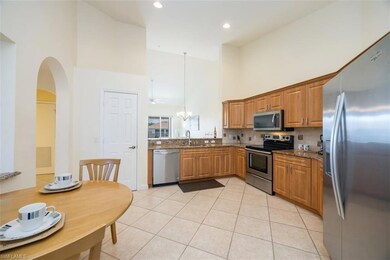 Kitchen with appliances with stainless steel finishes, a towering ceiling, light tile patterned flooring, decorative backsplash, and hanging light fixtures