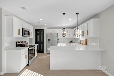 Kitchen featuring appliances with stainless steel finishes, a peninsula, light tile patterned floors, white cabinets, and pendant lighting