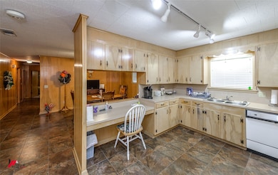 Kitchen with light countertops, a sink, wooden walls, visible vents, and dishwasher