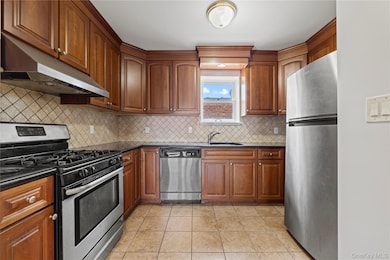 Kitchen with appliances with stainless steel finishes, under cabinet range hood, dark countertops, backsplash, and light tile patterned floors