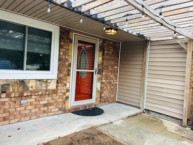 Doorway to property featuring a patio area, a pergola, and brick siding