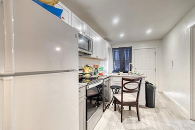Kitchen featuring stainless steel appliances, light wood finished floors, white cabinets, a peninsula, and light stone countertops