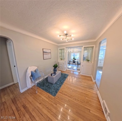 Living area featuring arched walkways, light wood finished floors, a textured ceiling, and a chandelier