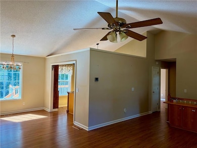 Unfurnished room with a textured ceiling, dark wood-style floors, a chandelier, high vaulted ceiling, and a ceiling fan