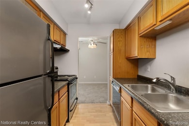 Kitchen with black appliances, light wood-style flooring, brown cabinetry, and under cabinet range hood