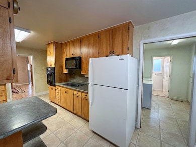 Kitchen with black appliances, dark countertops, brown cabinetry, and tasteful backsplash