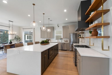Kitchen featuring high end appliances, light stone counters, backsplash, open shelves, and light wood finished floors