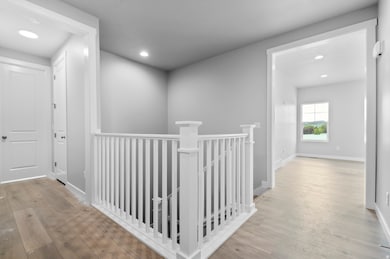 Corridor with an upstairs landing, light wood-type flooring, and recessed lighting