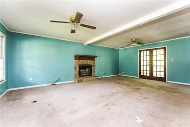Unfurnished living room featuring ceiling fan, a stone fireplace, baseboards, and ornamental molding