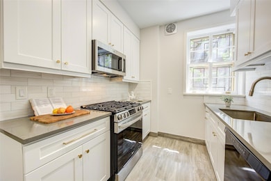 Kitchen featuring stainless steel appliances, a sink, backsplash, baseboards, and white cabinetry