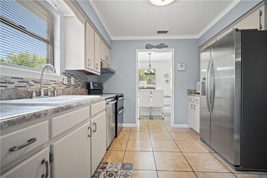 Kitchen with appliances with stainless steel finishes, ornamental molding, backsplash, light tile patterned flooring, and white cabinetry