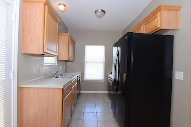 Kitchen with black fridge, light brown cabinetry,