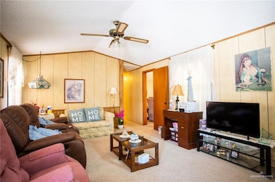 Living room featuring a ceiling fan, carpet floors, wooden walls, a textured ceiling, and lofted ceiling