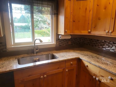 Kitchen with backsplash, brown cabinetry, and light stone counters
