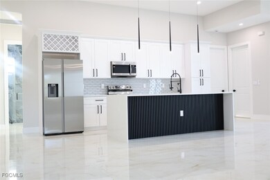 Kitchen with stainless steel appliances, tasteful backsplash, white cabinets, and an island with sink