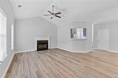 Unfurnished living room with ceiling fan, light wood-style flooring, a fireplace with raised hearth, vaulted ceiling, and ornamental molding