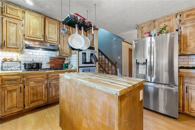 Kitchen with island, butcher block counters, under cabinet range hood,  multiple ovens