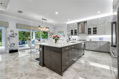 Kitchen featuring a center island with sink, light marble finish floors, pendant lighting, ornamental molding, and glass insert cabinets