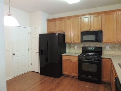 Kitchen featuring black appliances, dark wood-type flooring, light countertops, tasteful backsplash, and hanging light fixtures