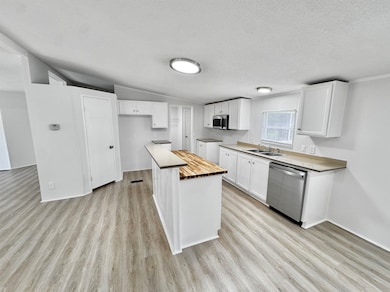 Kitchen featuring appliances with stainless steel finishes, wood counters, light wood-style flooring, white cabinets, and a textured ceiling