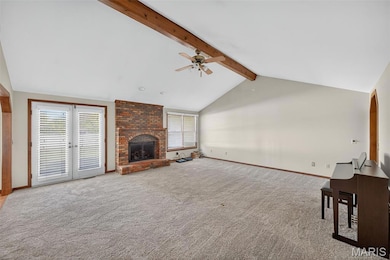 Unfurnished living room with plenty of natural light, beamed ceiling, carpet flooring, a brick fireplace, and a ceiling fan
