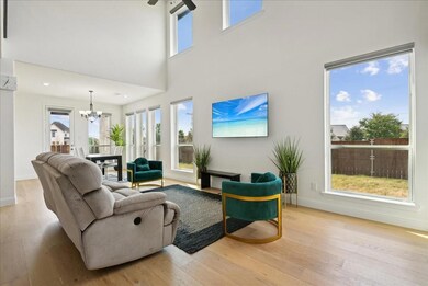 Living area with a notable chandelier, light wood-style flooring, baseboards, and a towering ceiling