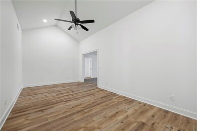 Empty room with a ceiling fan, high vaulted ceiling, wood finished floors, and baseboards