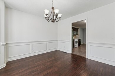 Dining area with a chandelier, dark wood-style flooring, wainscoting, and a decorative wall