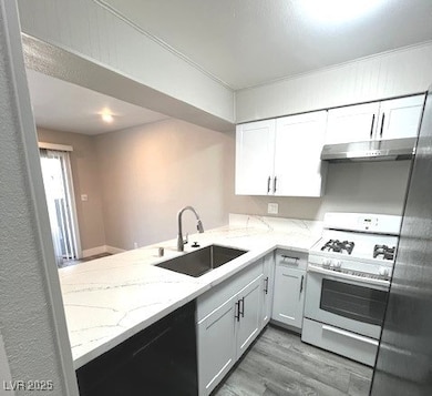 Kitchen featuring white gas range, a peninsula, under cabinet range hood, white cabinets, and light wood finished floors
