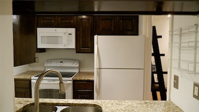 Kitchen featuring dark brown cabinetry, granite countertops, and white appliances