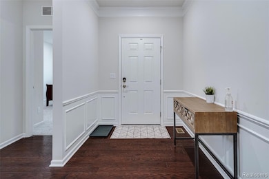 Entrance foyer featuring crown molding, dark wood-style flooring, a decorative wall, and a wainscoted wall
