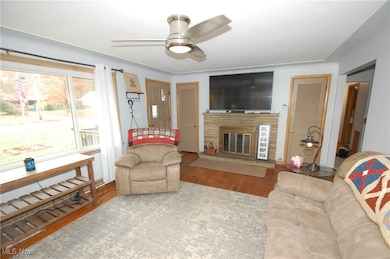 Living room featuring wood finished floors, a stone fireplace, and ceiling fan