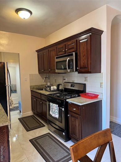 Kitchen with stainless steel stove, dark brown cabinets, decorative backsplash, light tile patterned floors, and fridge