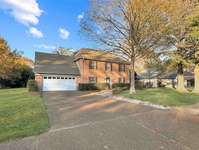 Colonial home with a front yard, concrete driveway, brick siding, and a garage