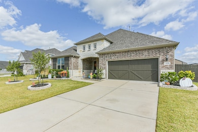 Clean concrete driveway leads to a two-car garage and a welcoming front porch. A circular stone planter anchors the yard, enhancing the landscape design.