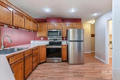 Kitchen featuring appliances with stainless steel finishes, a textured ceiling, light wood-style floors, brown cabinetry, and light countertops