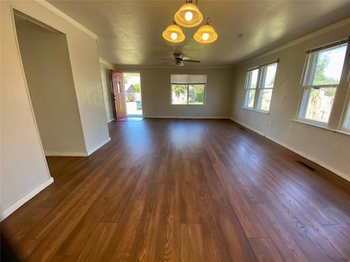 Empty room with dark wood-style floors, crown molding, and ceiling fan