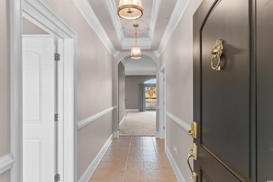 Hallway with a raised ceiling, arched walkways, ornamental molding, light colored carpet, and light tile patterned floors
