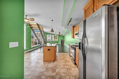 Kitchen with appliances with stainless steel finishes, a kitchen island, light wood-type flooring, ceiling fan, and decorative light fixtures