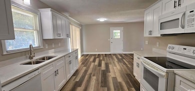 Kitchen featuring white appliances, a textured ceiling, dark wood finished floors, white cabinetry, and light stone counters