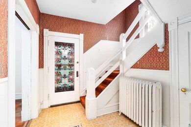 Entrance foyer with wallpapered walls, radiator heating unit, a wainscoted wall, and stairs